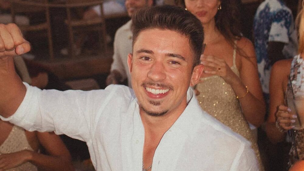 Um homem sorri numa festa com outras pessoas