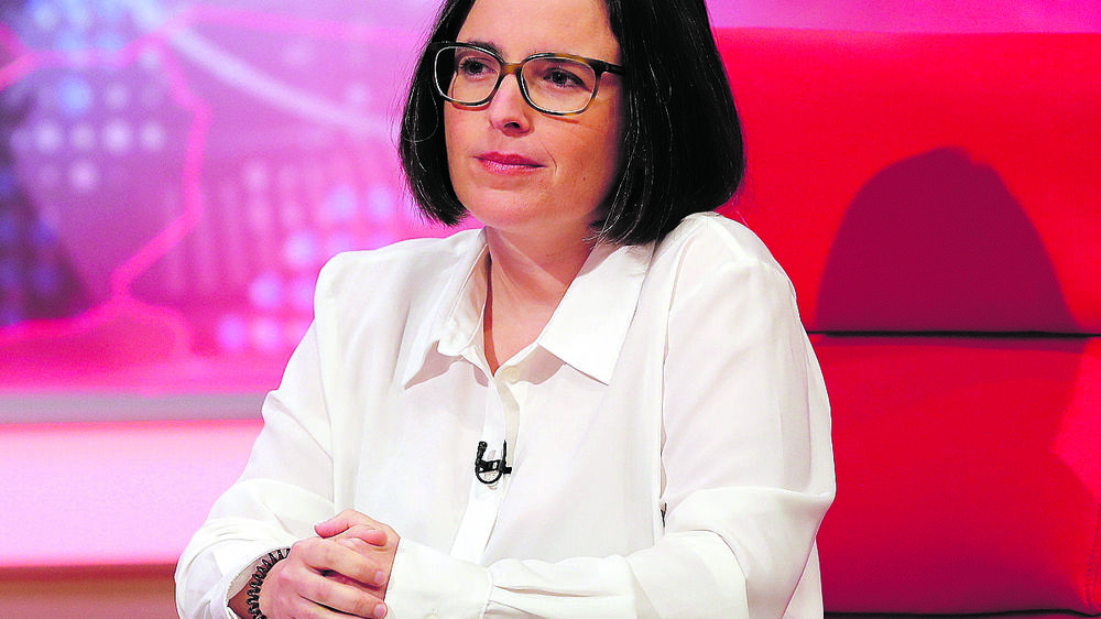 Mulher de óculos e camisa branca sentada numa mesa vermelha