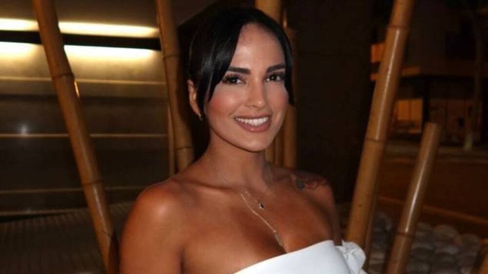Mulher sorri num evento com vestido branco e colar