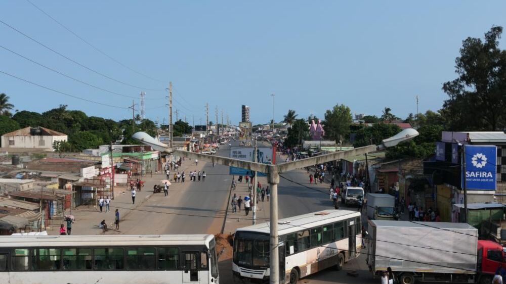Rua movimentada em Maputo com pessoas, autocarros e edifícios