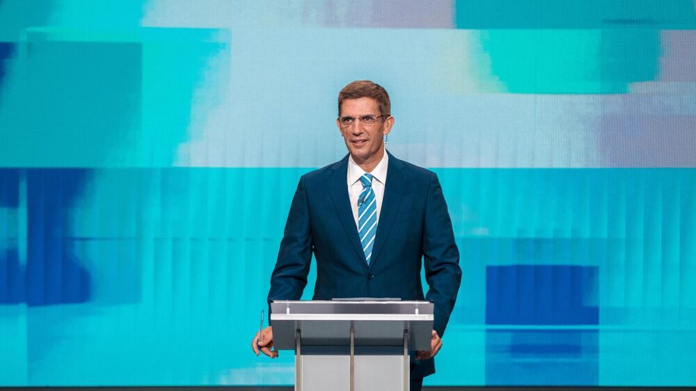 Um homem de fato e gravata discursa num pódio