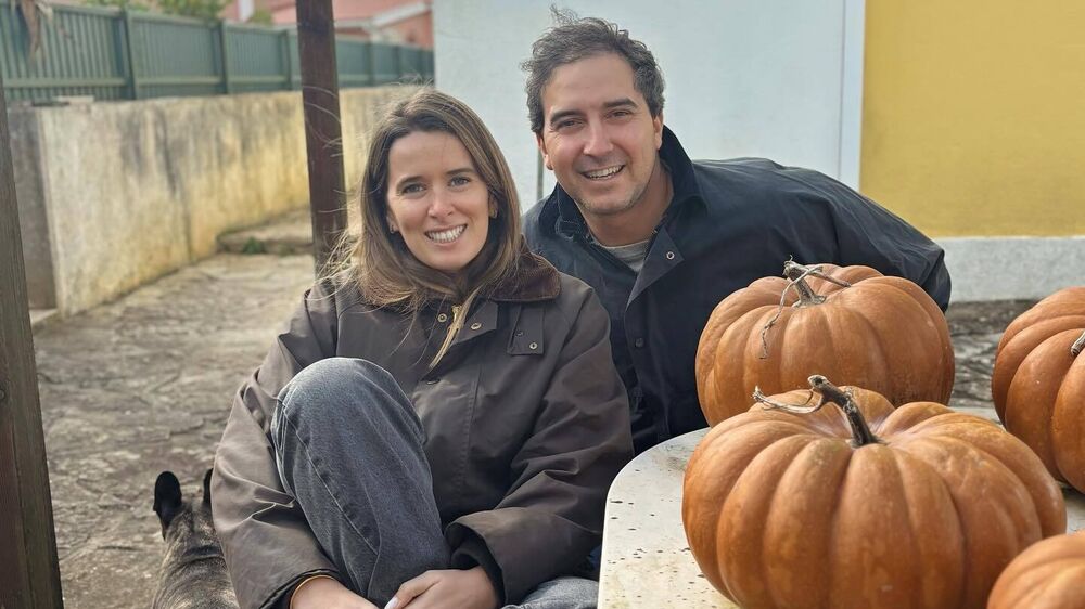 Casal sorri junto a abóboras e cão num espaço exterior