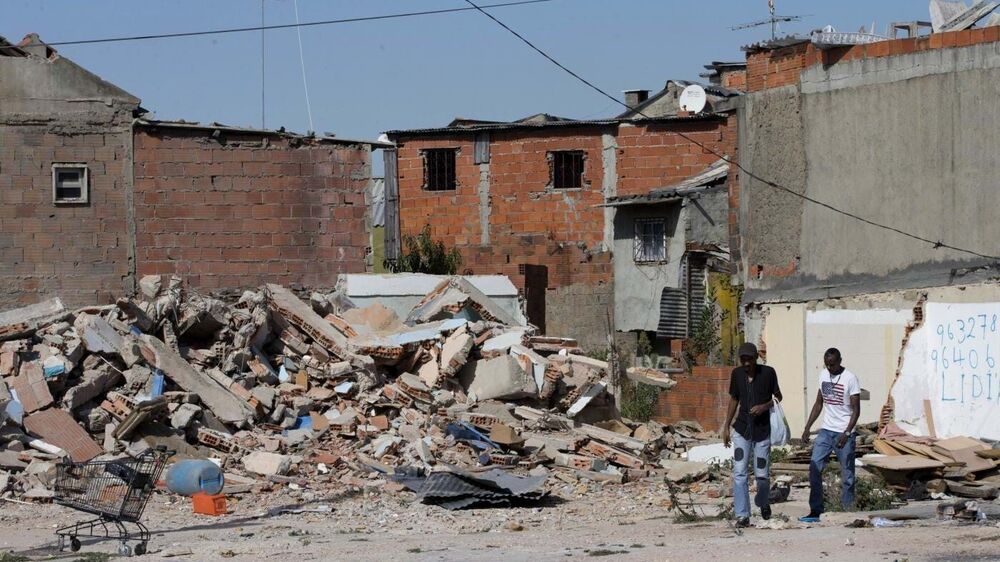 Ruínas de edifícios danificados e pessoas a caminhar numa zona urbana