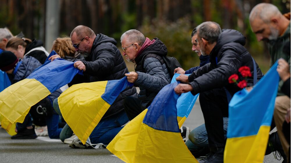 Pessoas ajoelhadas com a bandeira da Ucrânia em homenagem aos soldados mortos