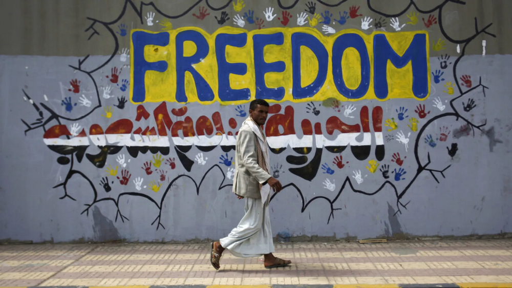 Um homem caminha em frente a um mural com a palavra 'Liberdade'