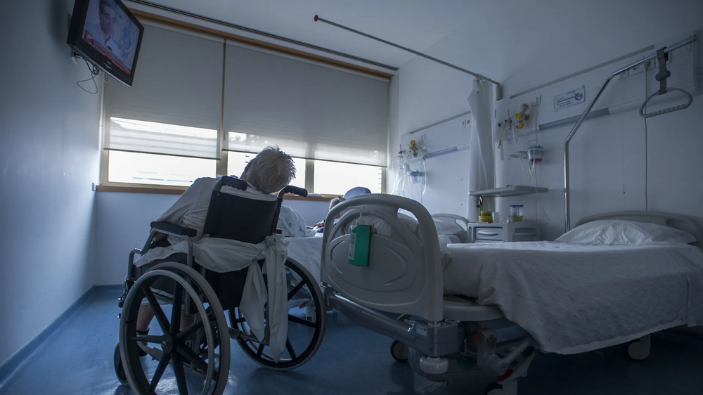 Doente em cadeira de rodas num quarto de hospital do SNS, aguardando reabilitação 
